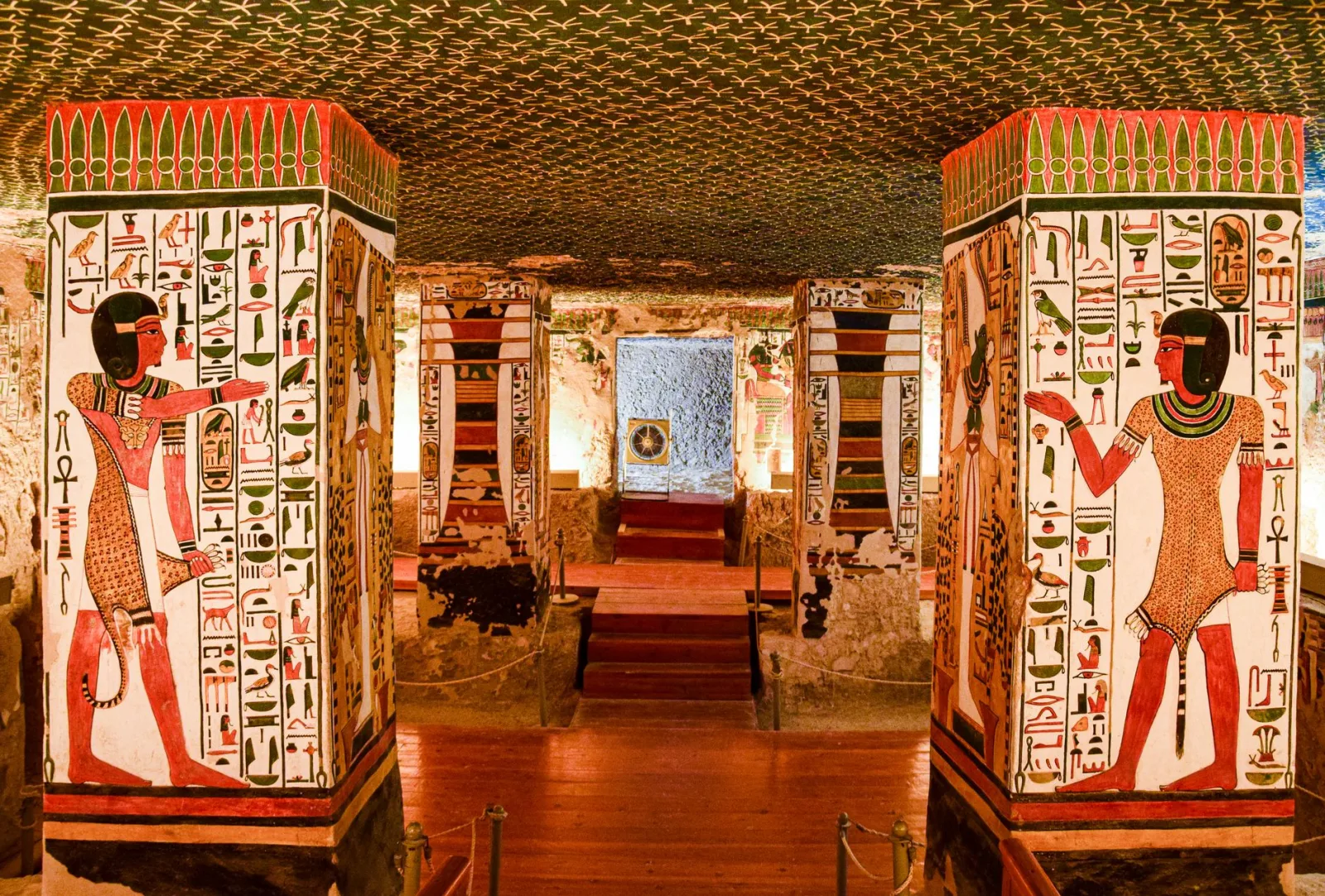 Interior of an ancient Egyptian tomb featuring vividly painted columns with hieroglyphics and murals.