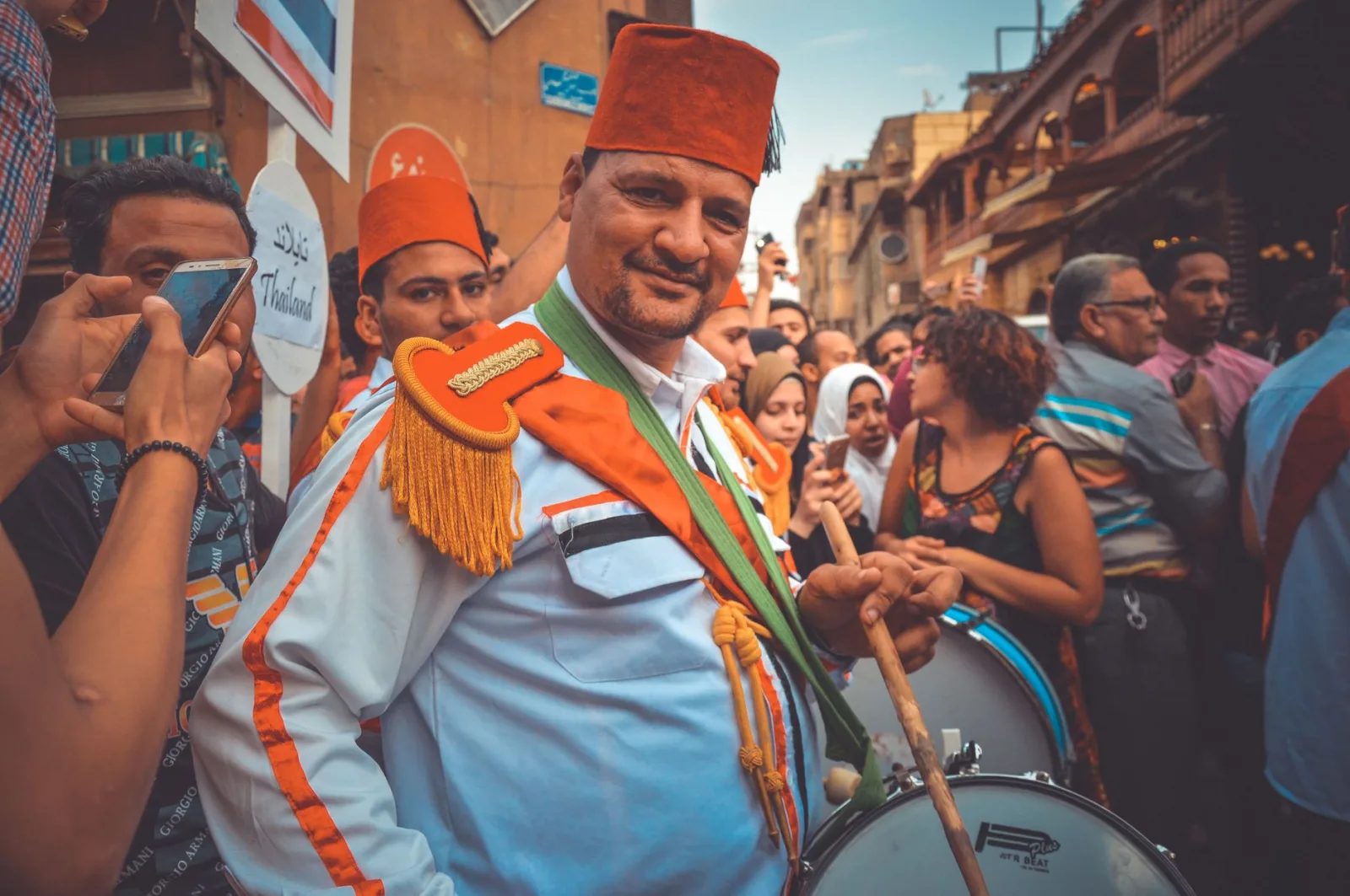 Man in traditional attire playing drums at a lively Cairo street festival.