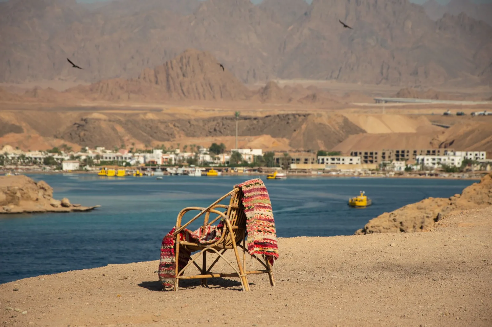 A chair draped with a colorful blanket overlooks a serene desert coastline.