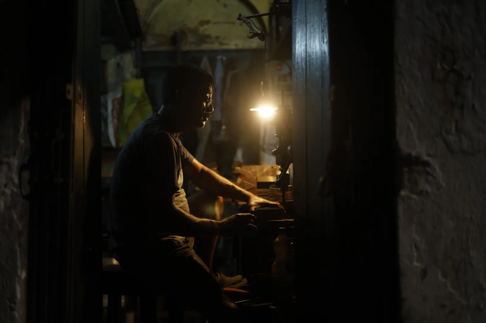 Artisan in dim workshop focuses under warm light, showcasing dedication and craftsmanship.