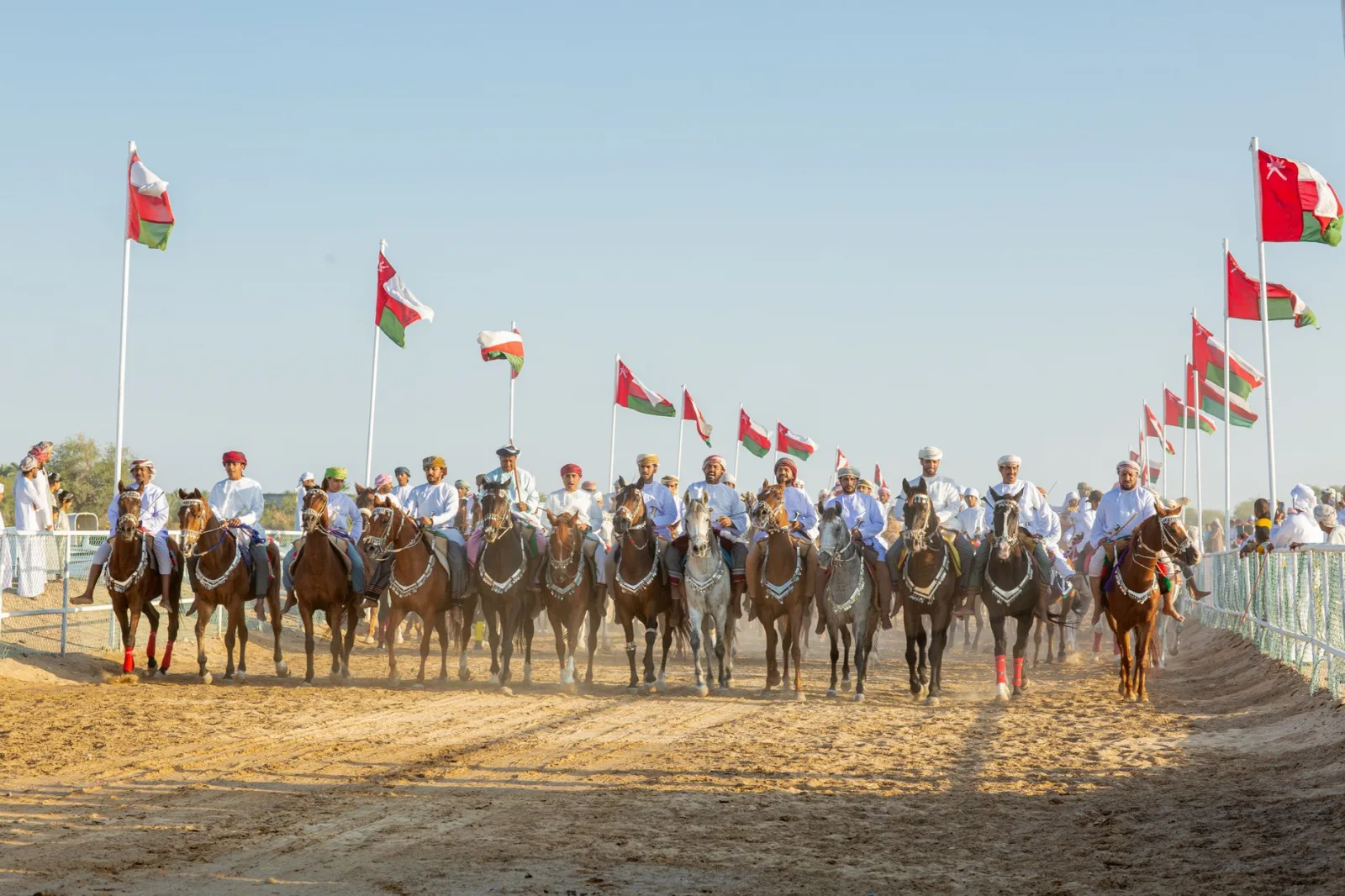 A cultural horse parade with riders in traditional dress and turbans, set against a clear blue sky.