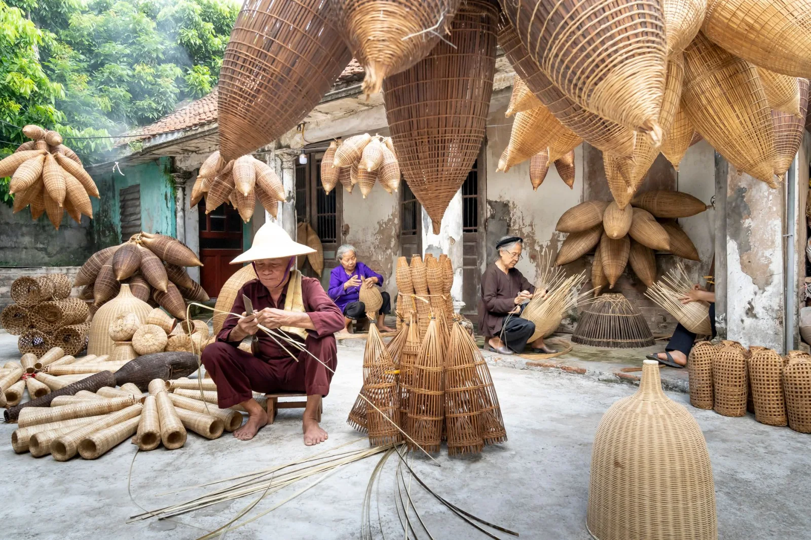 Elderly artisans crafting traditional bamboo fish traps in a sunlit courtyard.
