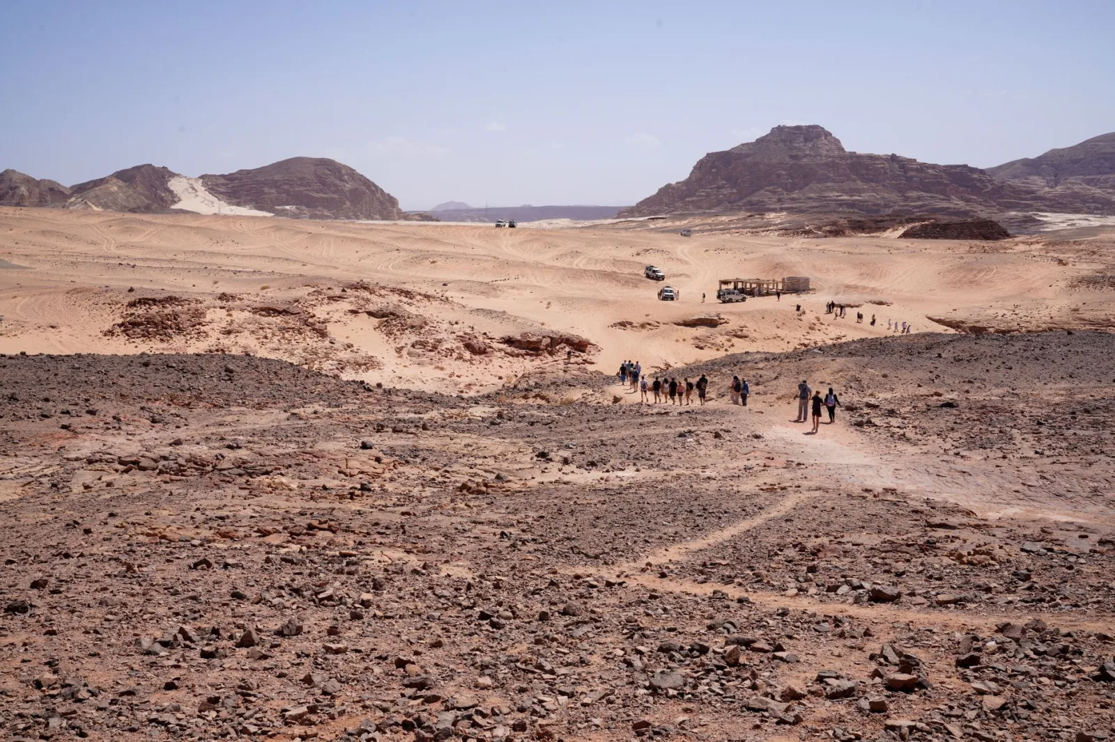A group of explorers walking through the rugged terrain of the Egyptian desert under clear blue skies.