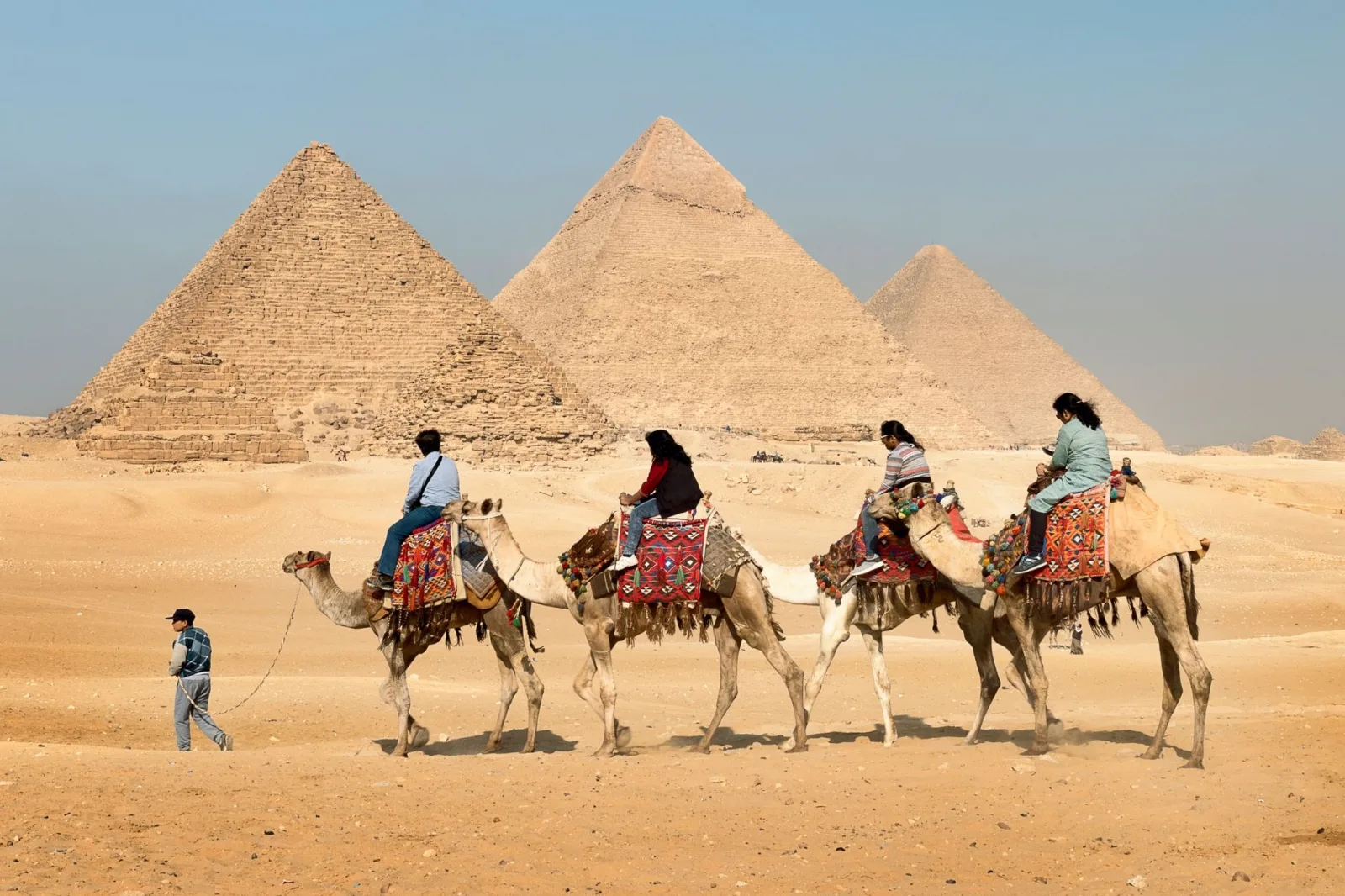 Tourists riding camels near the Great Pyramids of Giza, Egypt under clear skies.