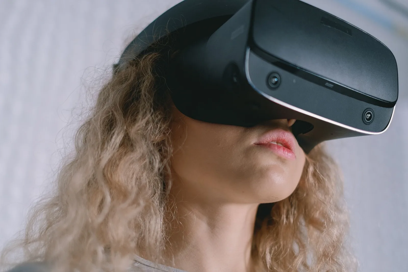 A young woman with curly hair using a VR headset, experiencing virtual reality.