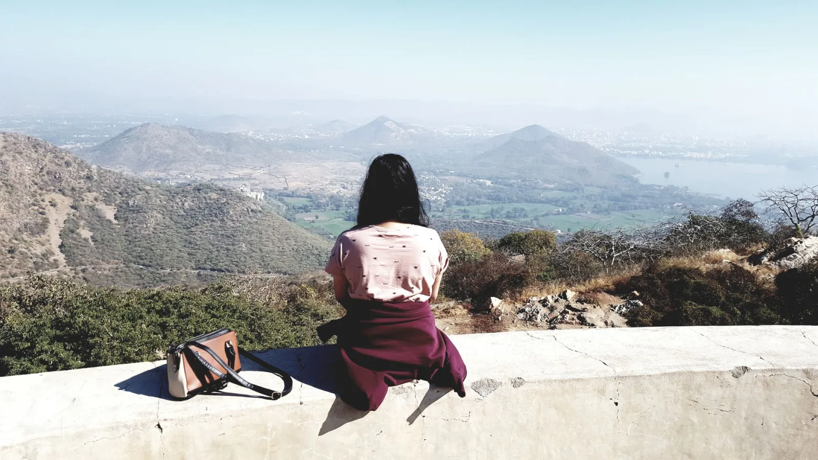 A woman sits on a wall, overlooking the scenic landscape of Kodiyat, India.