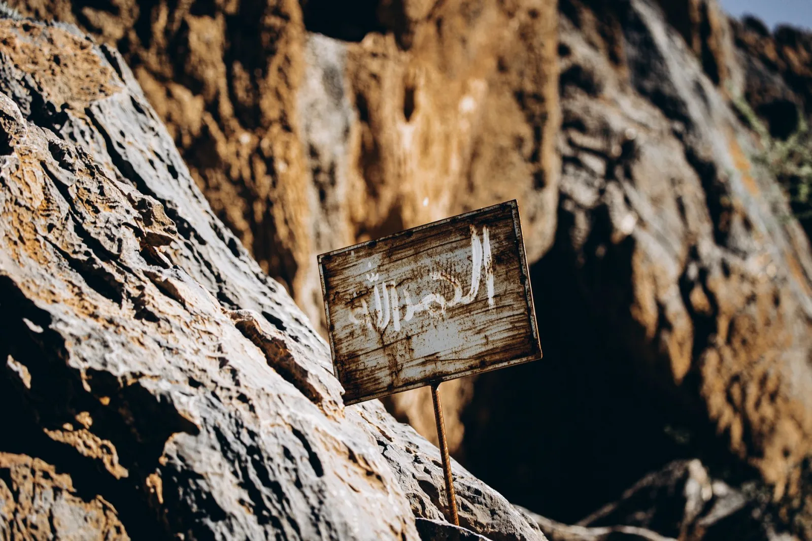 A close-up of a weathered sign in the rugged terrain of the Omani desert.