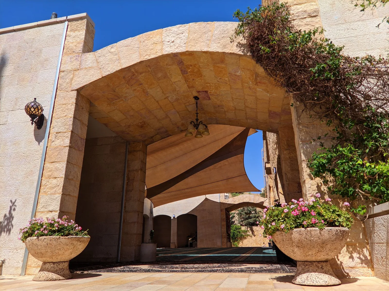 Charming stone archway in Amman adorned with sunlit flowers and greenery, creating a serene, architectural view.