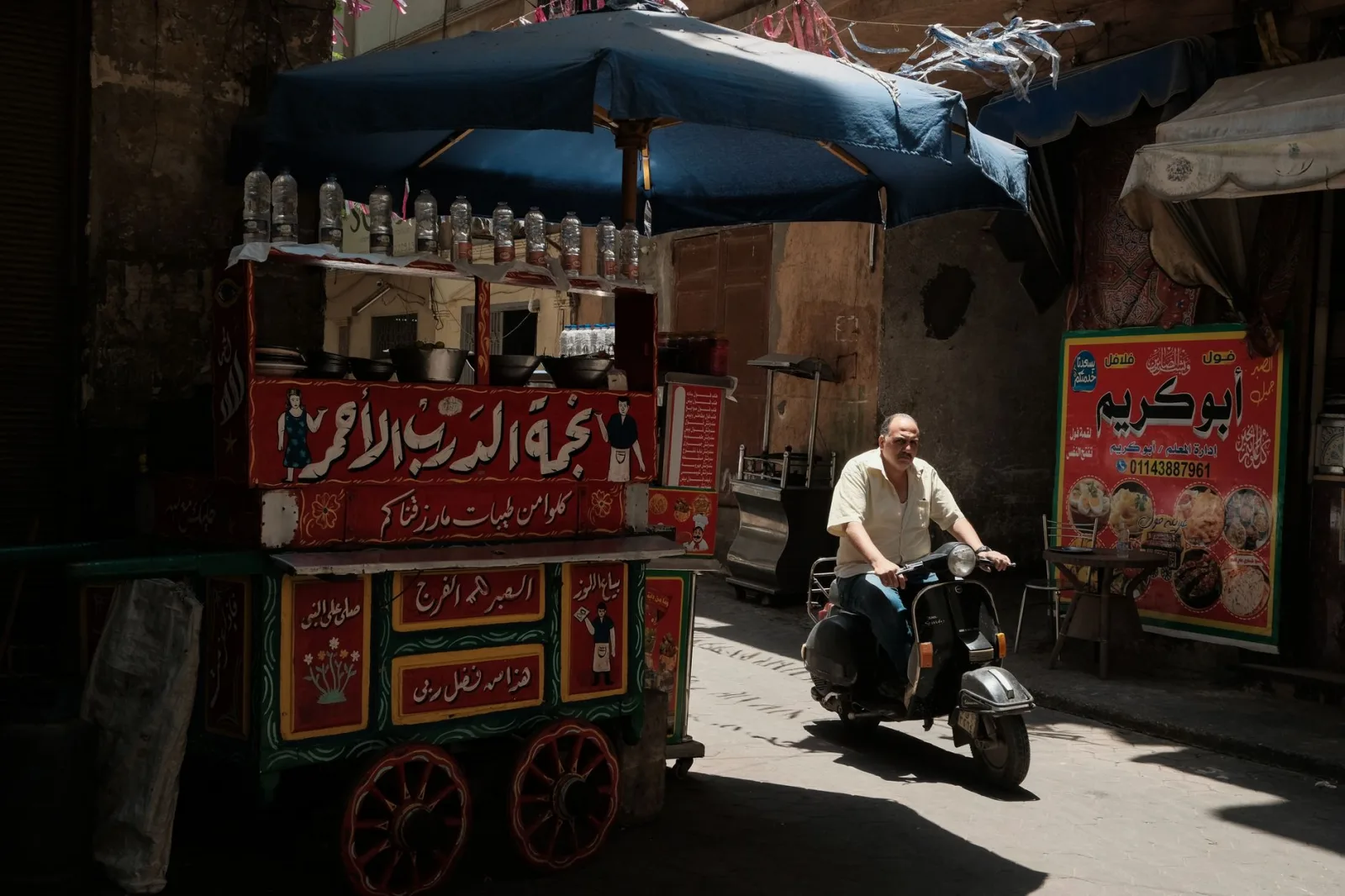 Traditional Egyptian street food cart with a man riding a scooter in Cairo's vibrant alley.