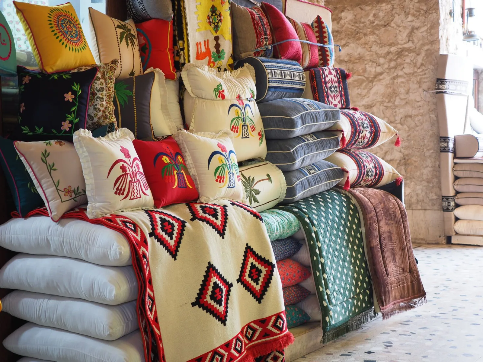 Vibrant embroidered cushions and textiles on display in a Doha market.
