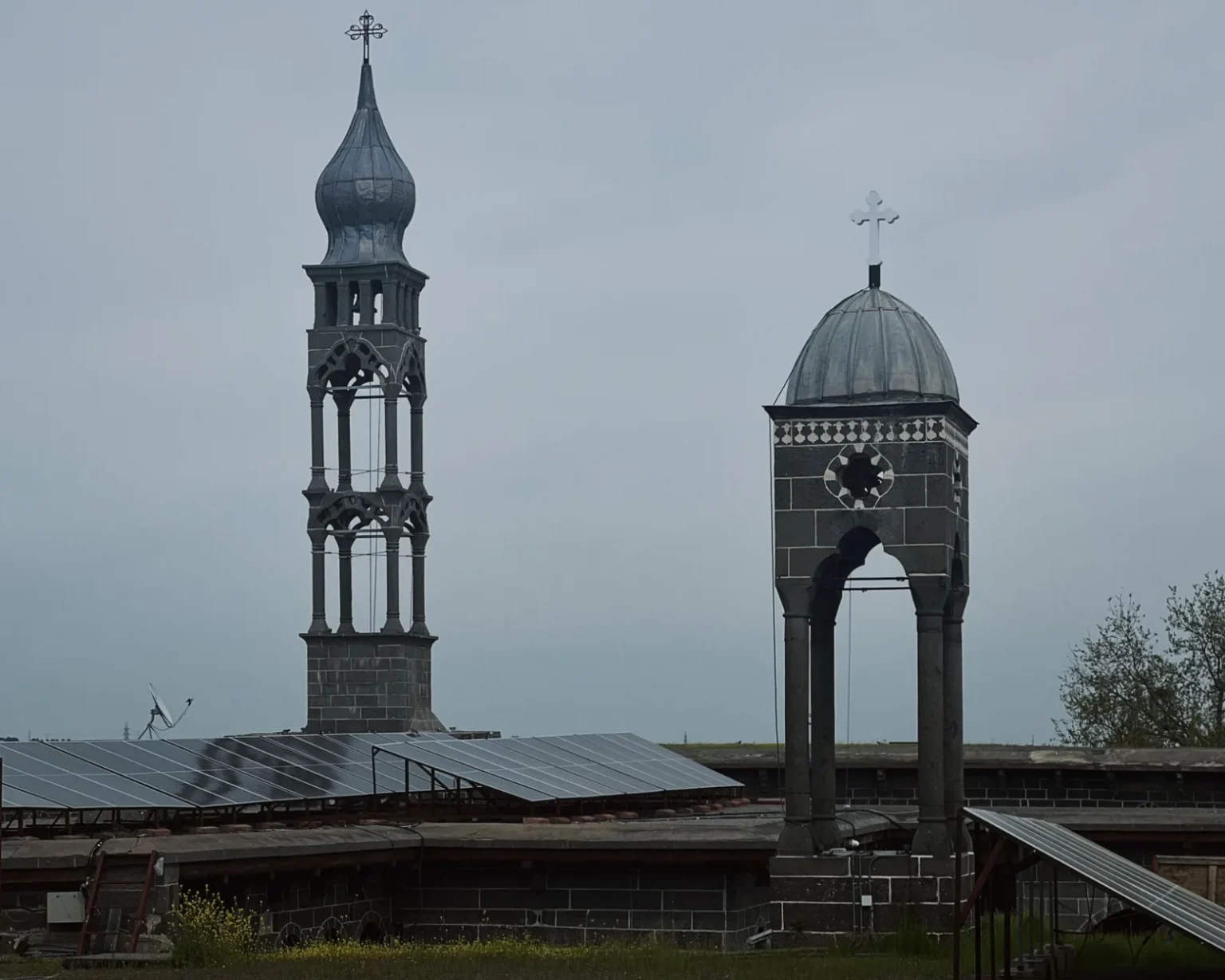 Ancient church towers juxtaposed with modern solar panels under a cloudy sky.
