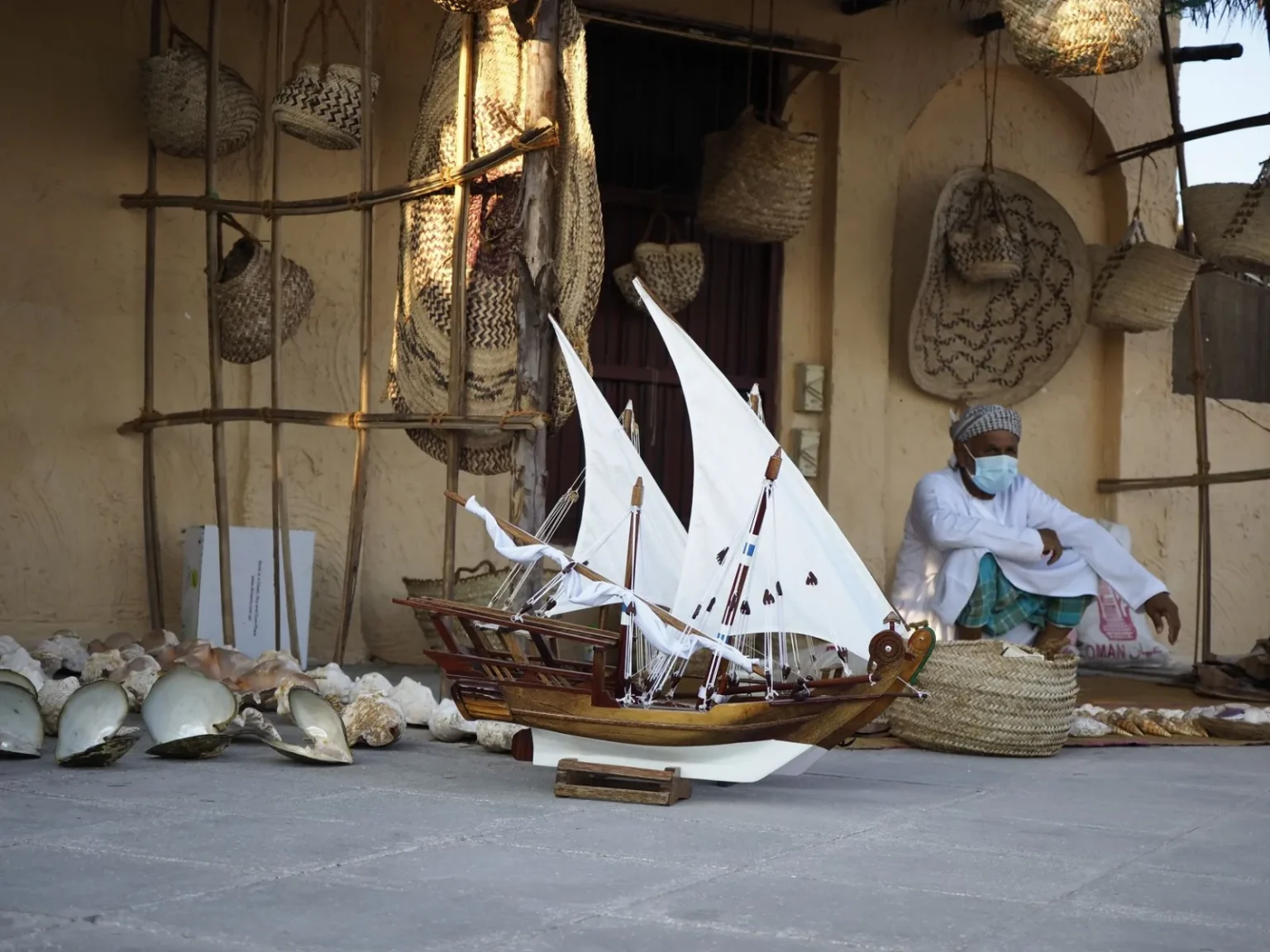 A man in traditional attire with a model dhow boat in a Doha marketplace setting.