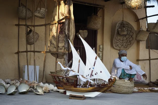 A man in traditional attire with a model dhow boat in a Doha marketplace setting.