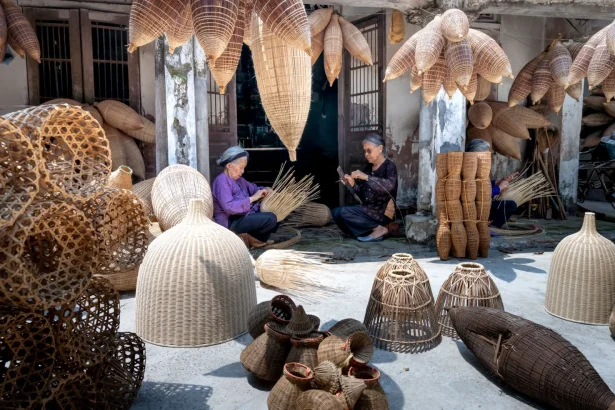 Aged ethnic women making bamboo traditional Vietnamese fish traps placed on ground and hanging in yard in sunlight