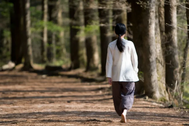 A woman walks barefoot along a peaceful forest path under sunlight, reflecting tranquility.
