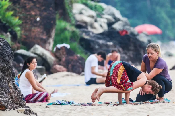 Women practicing yoga poses on sandy Varkala Beach in India, surrounded by natural beauty and vibrant colors.