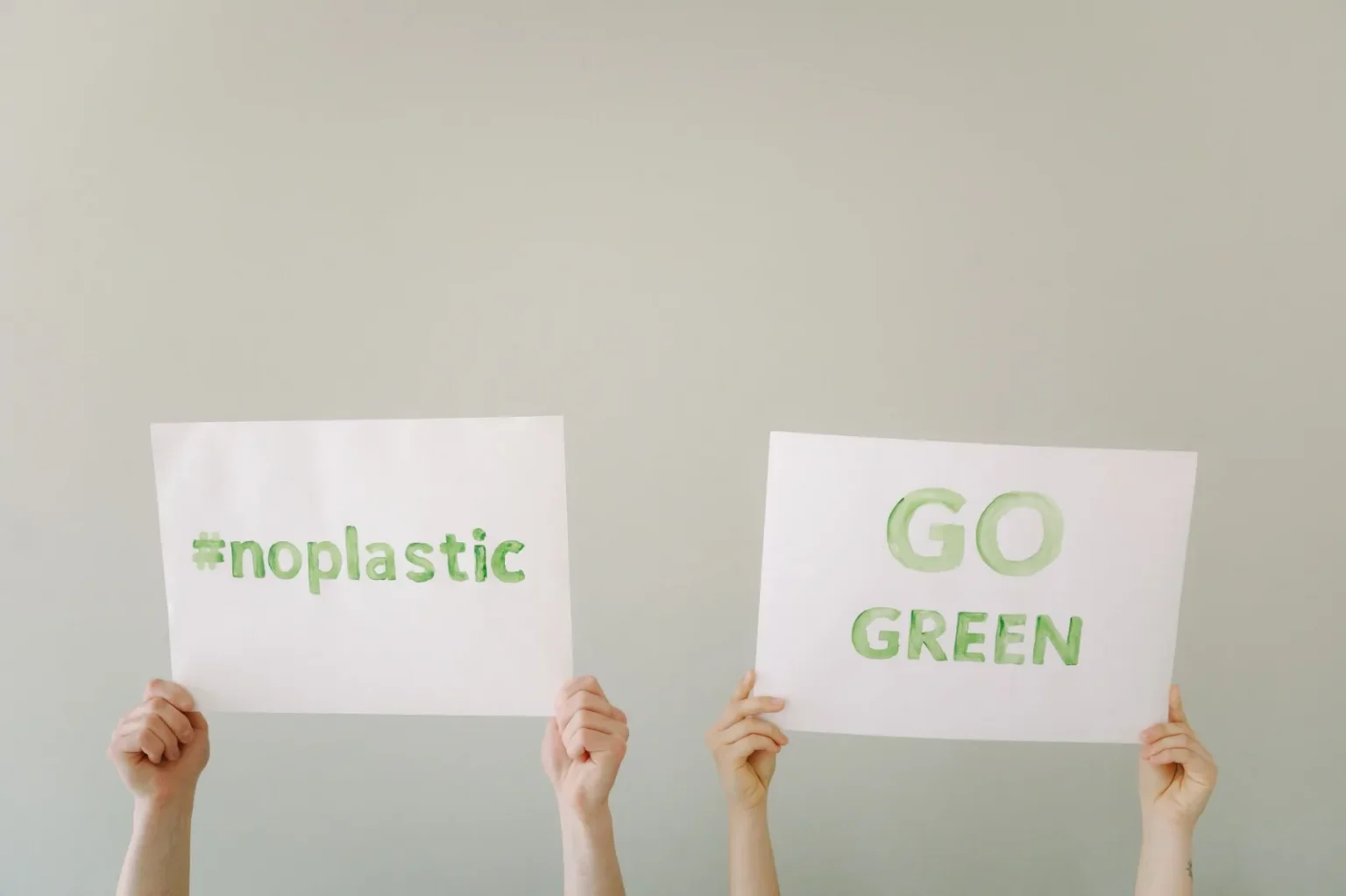 Hands holding eco-friendly signs advocating 'No Plastic' and 'Go Green'. Environmental awareness concept.
