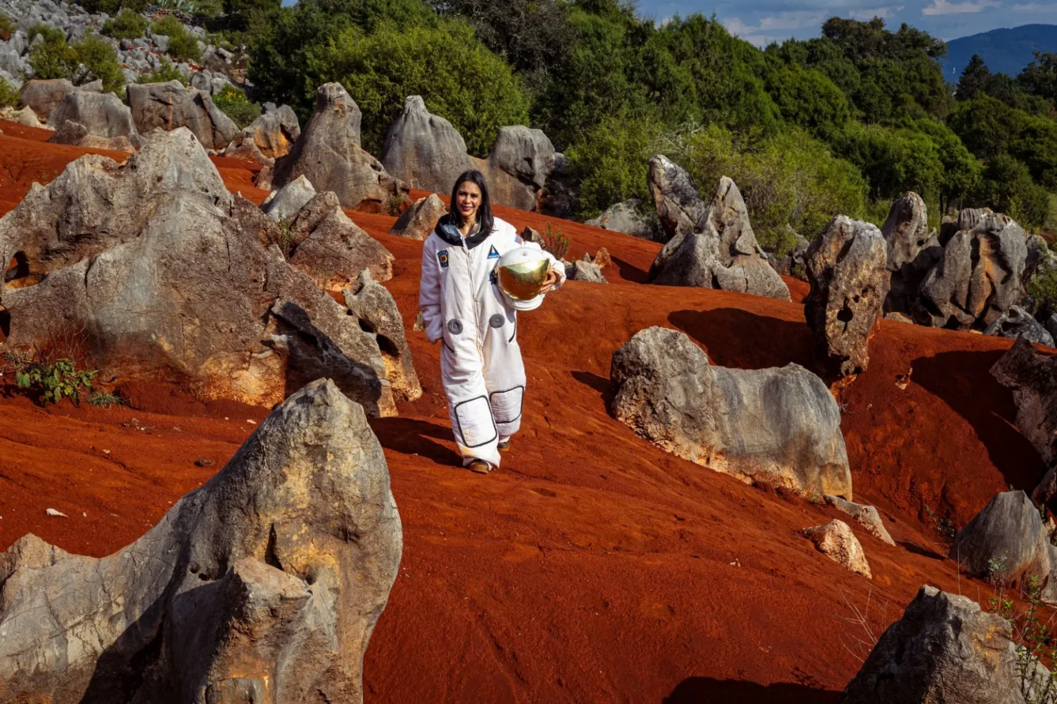Astronaut in space suit exploring rocky, earth-like terrain with red soil and greenery.