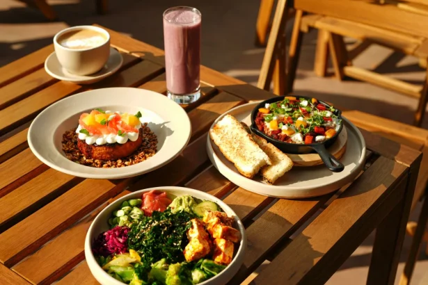 A vibrant set of healthy dishes including a smoothie and coffee on an outdoor wooden table.
