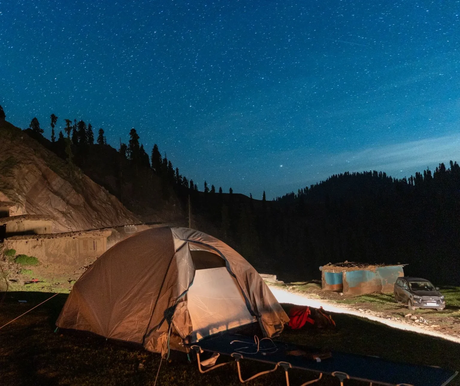 Camping in the mountains under a dazzling starry sky, featuring a lit tent and tranquil night scenery.