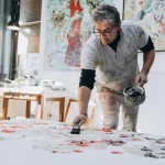 Adult male artist creating abstract artwork in a well-lit studio space, working passionately on a large canvas.