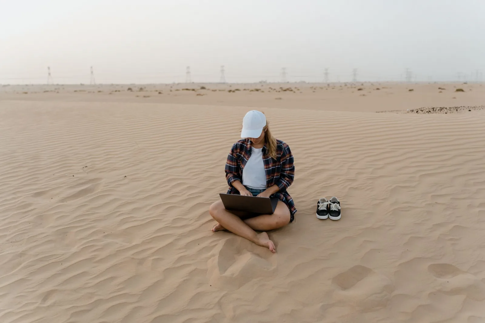 A woman in a desert using a laptop, symbolizing remote work freedom and digital nomad lifestyle.