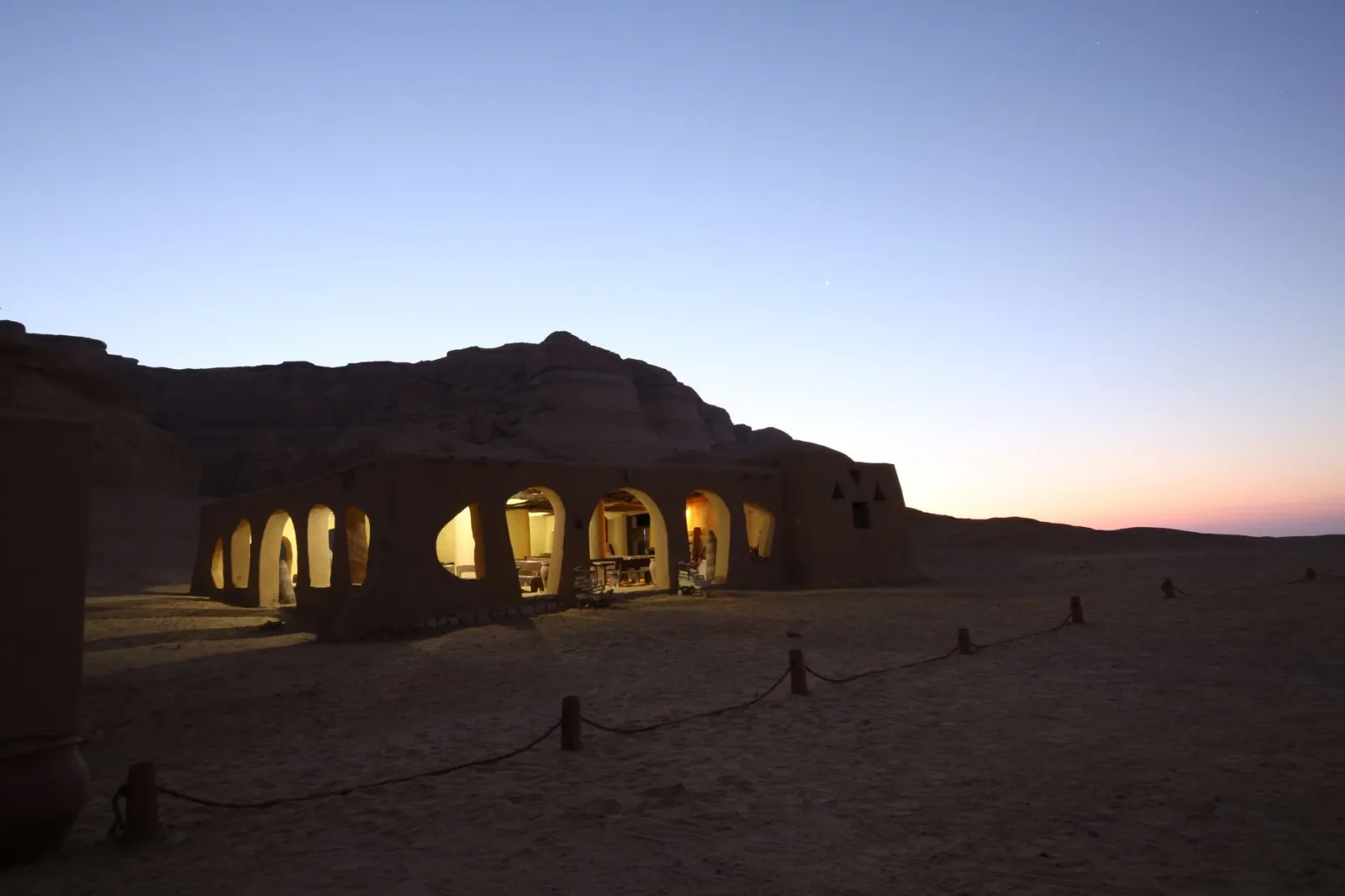 A serene desert gazebo illuminated from within at twilight, surrounded by vast sandscape.