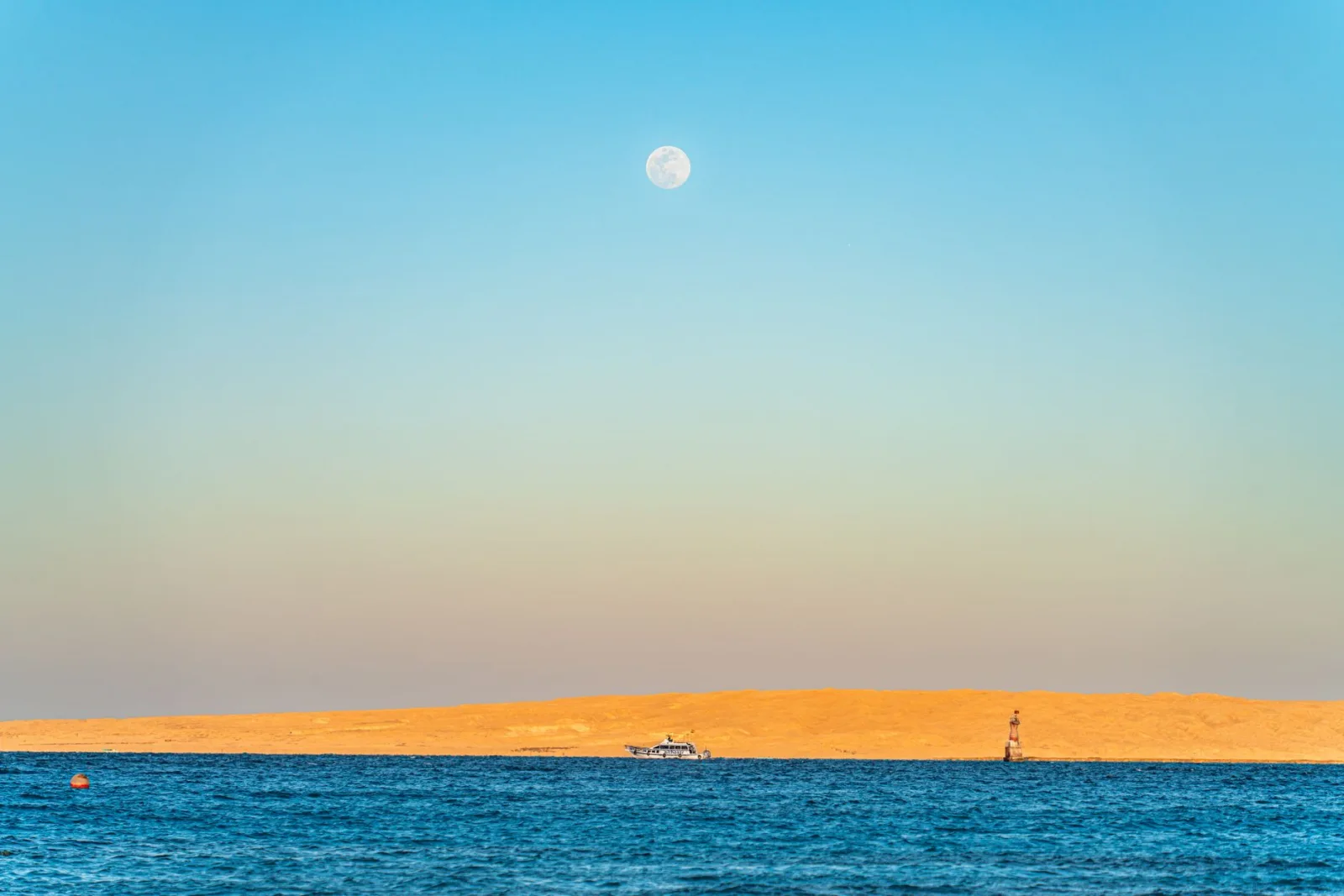 A serene view of the Red Sea in Hurghada, Egypt, with a full moon rising above golden sand dunes.