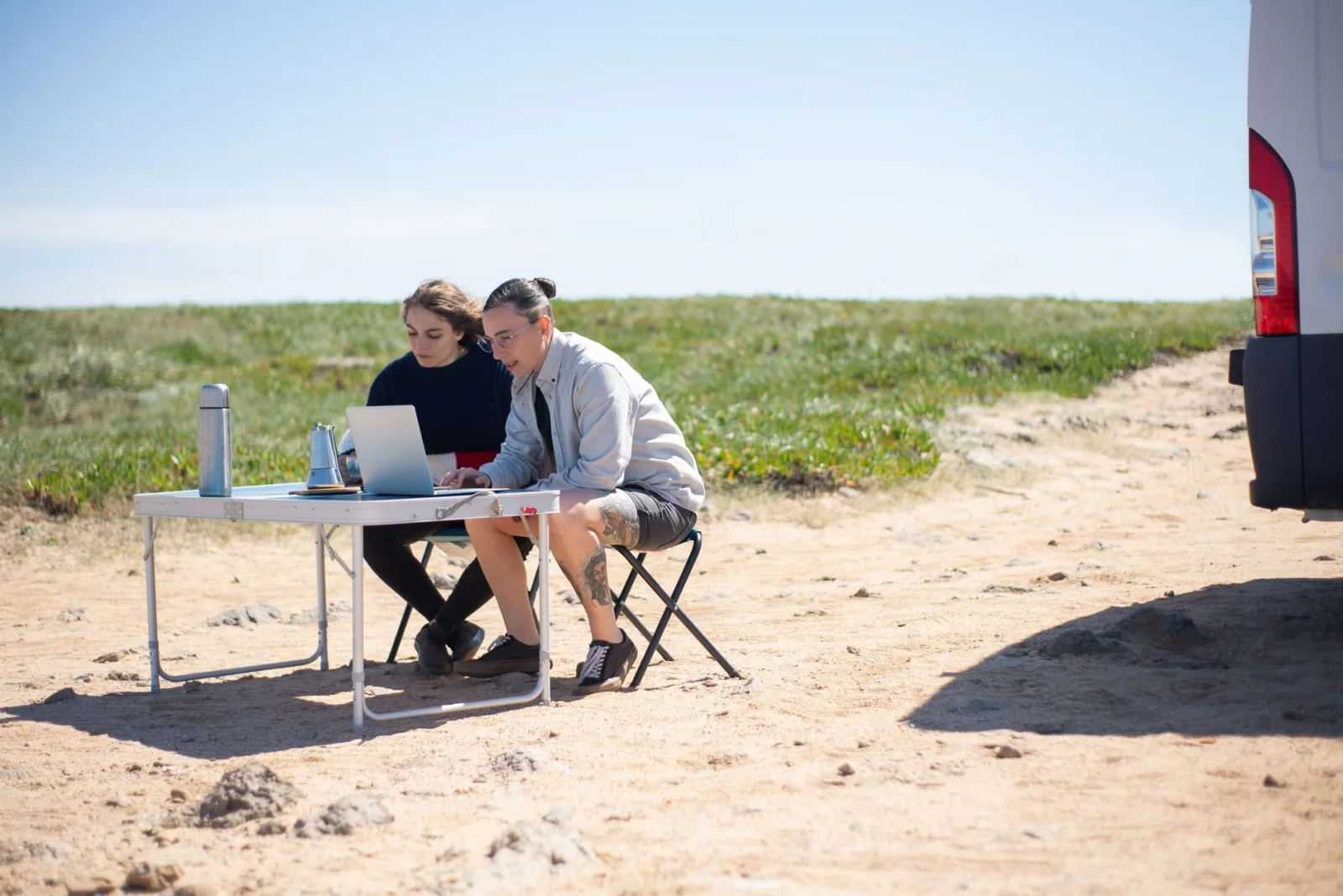 Two adults working on laptops outdoors in Portugal, enjoying a sunny day with portable workspace.