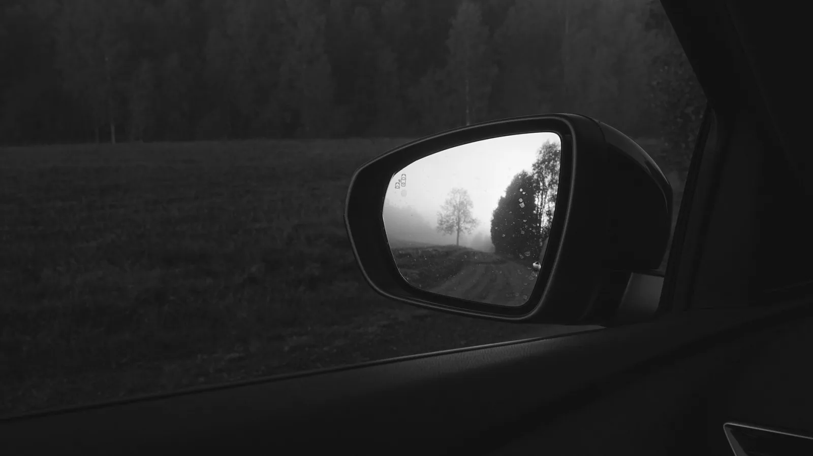 Monochrome side-view mirror reflection of a foggy landscape, adding mystery.