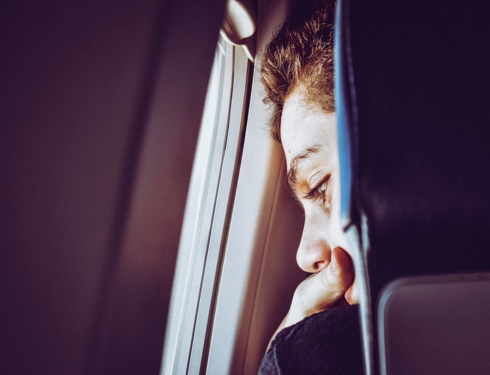 A young man looks thoughtfully out of an airplane window, captured in a close-up portrait.