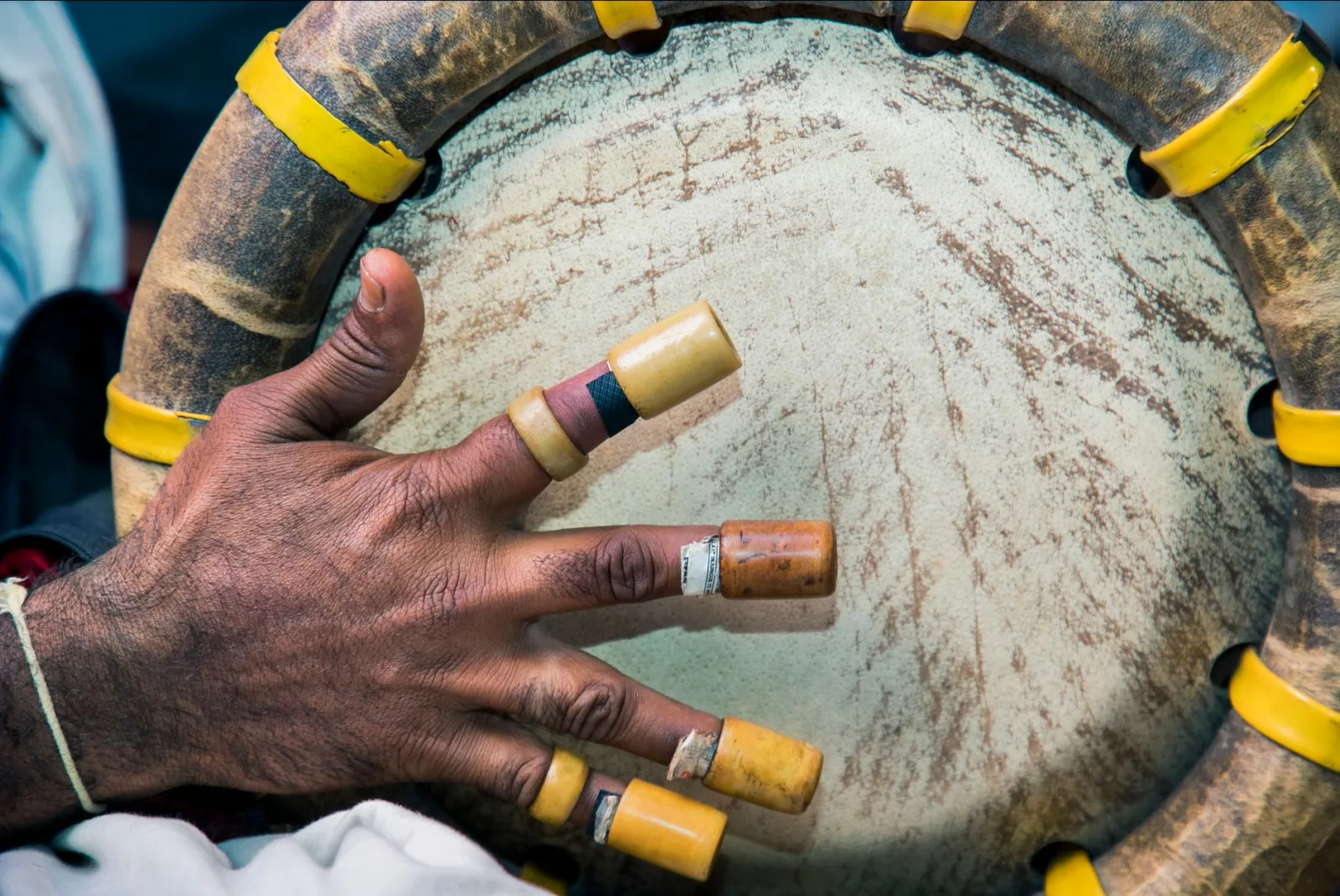 A detailed view of a hand with wrapped fingers playing a traditional drum, highlighting cultural music elements.