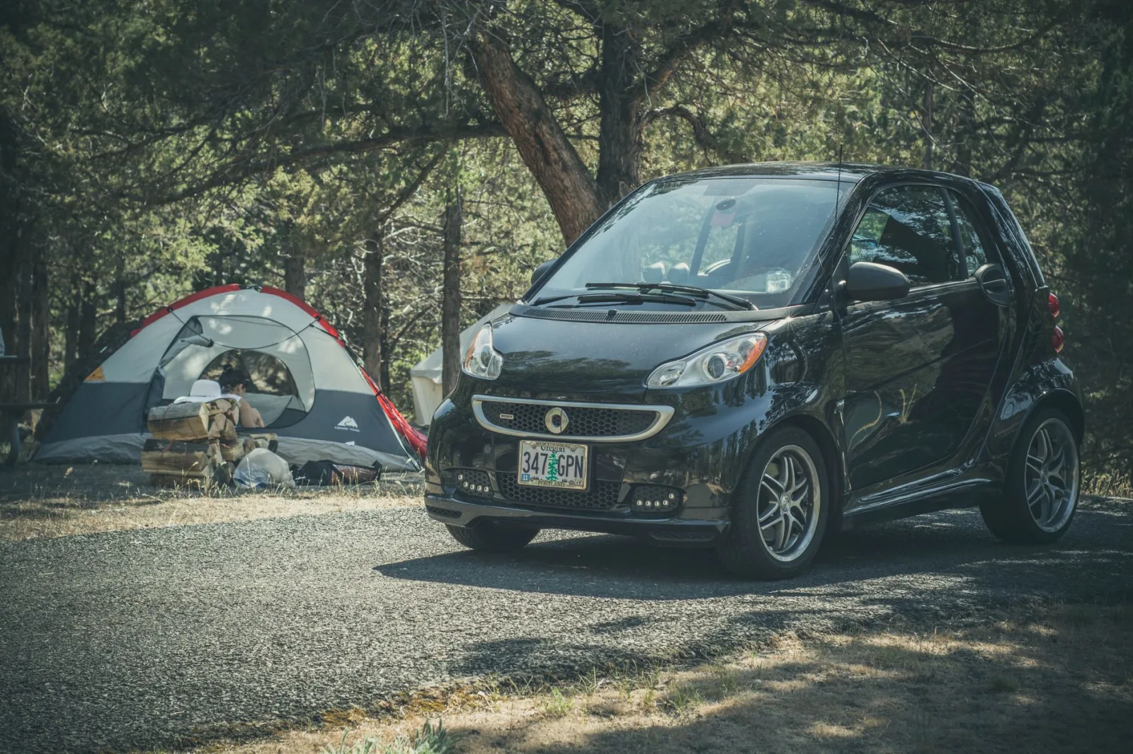 Smart car parked beside a tent in a wooded campsite, perfect for outdoor adventures.