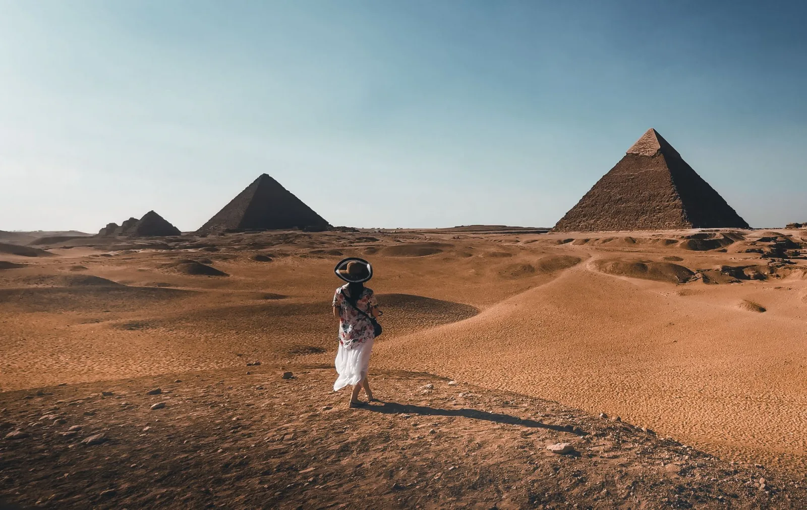 A woman stands in the Egyptian desert, with pyramids in the background.