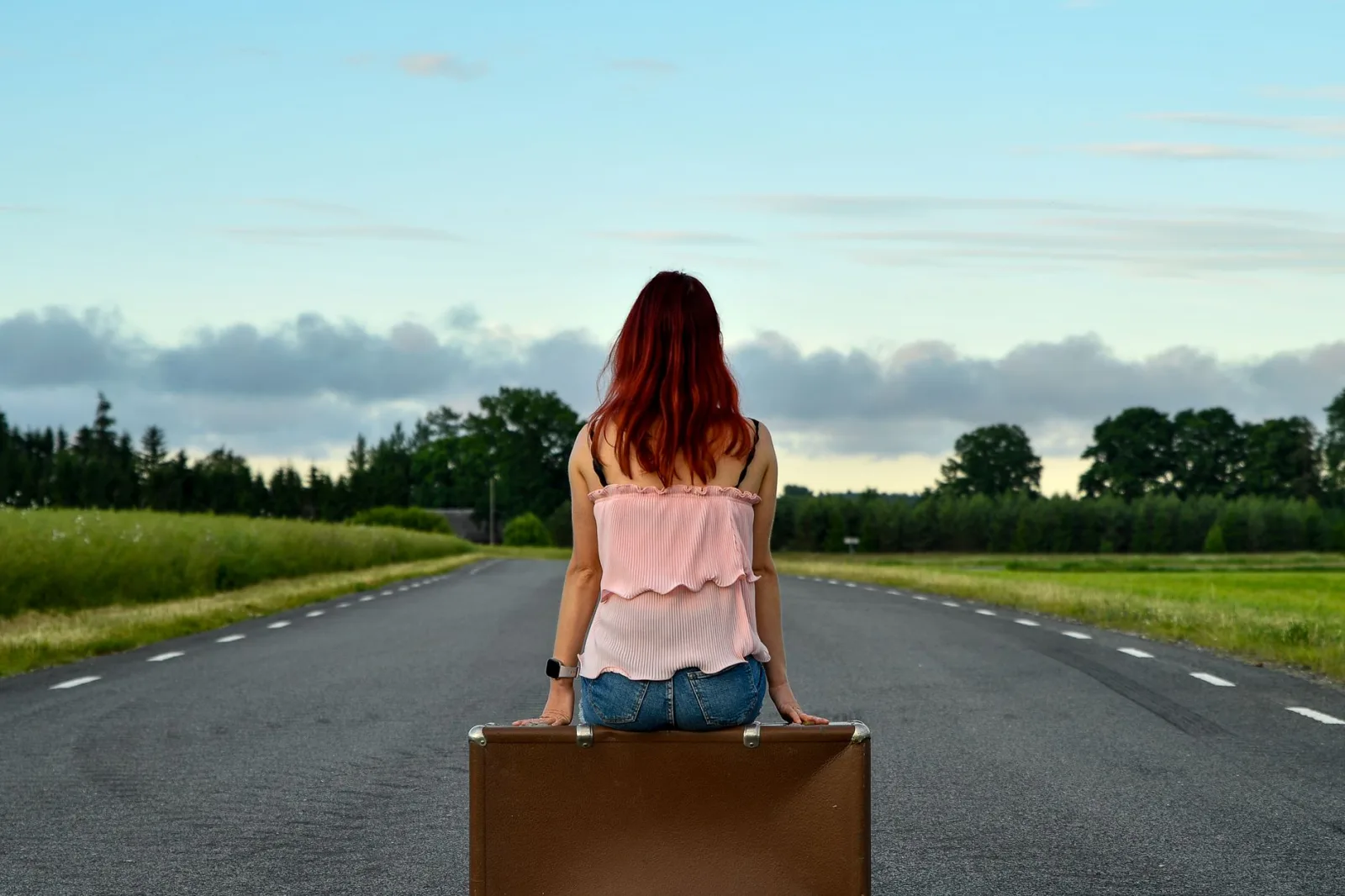 Woman sitting on suitcase in countryside, symbolizing travel and freedom.