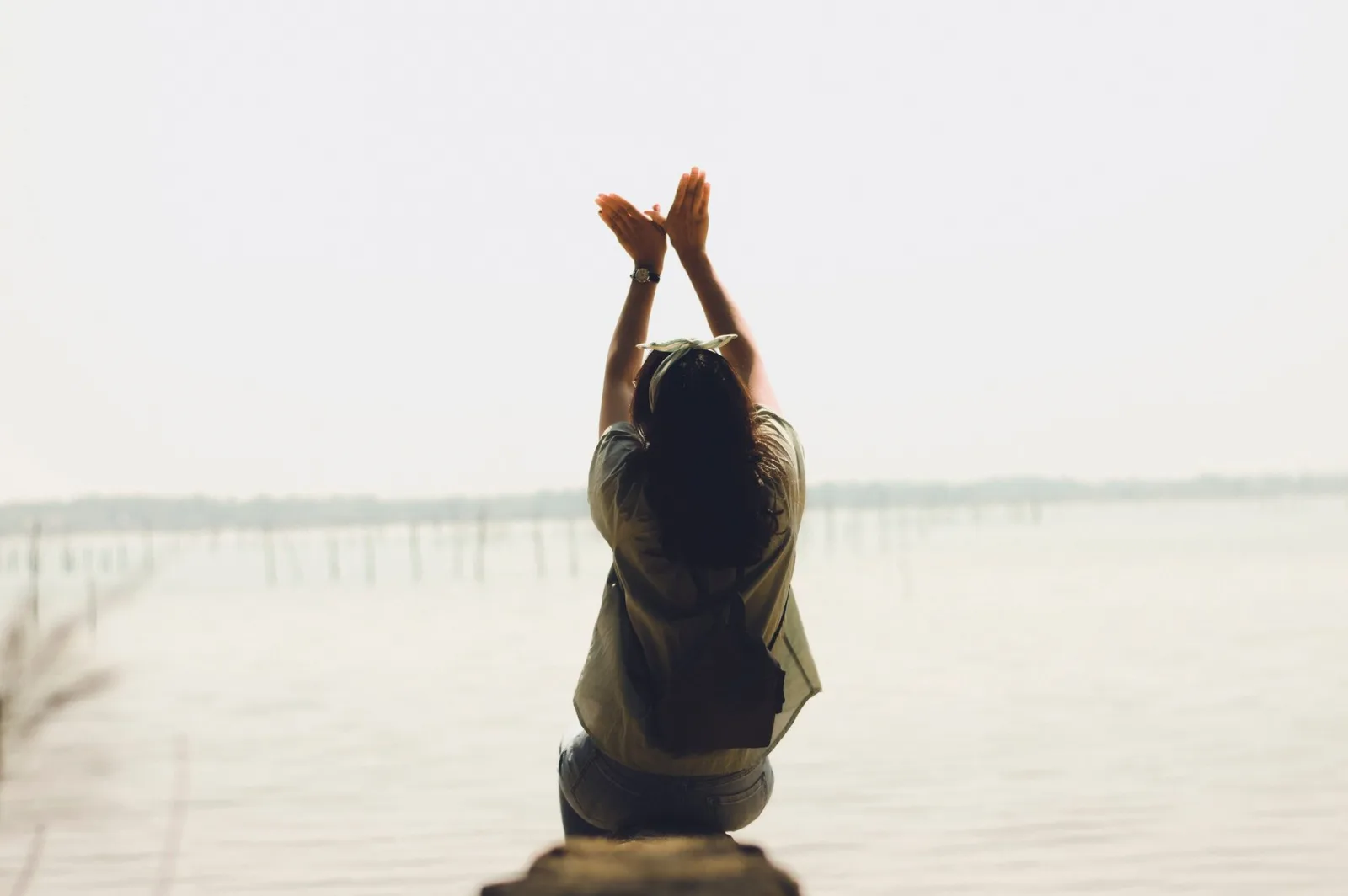 A serene moment of a woman raising her arms by a calm lake, embracing nature's tranquility.