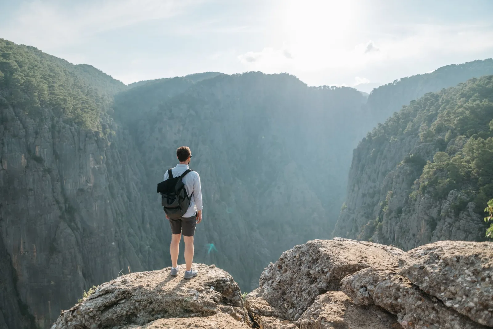 A man with a backpack overlooks a stunning mountain canyon on a sunny day.