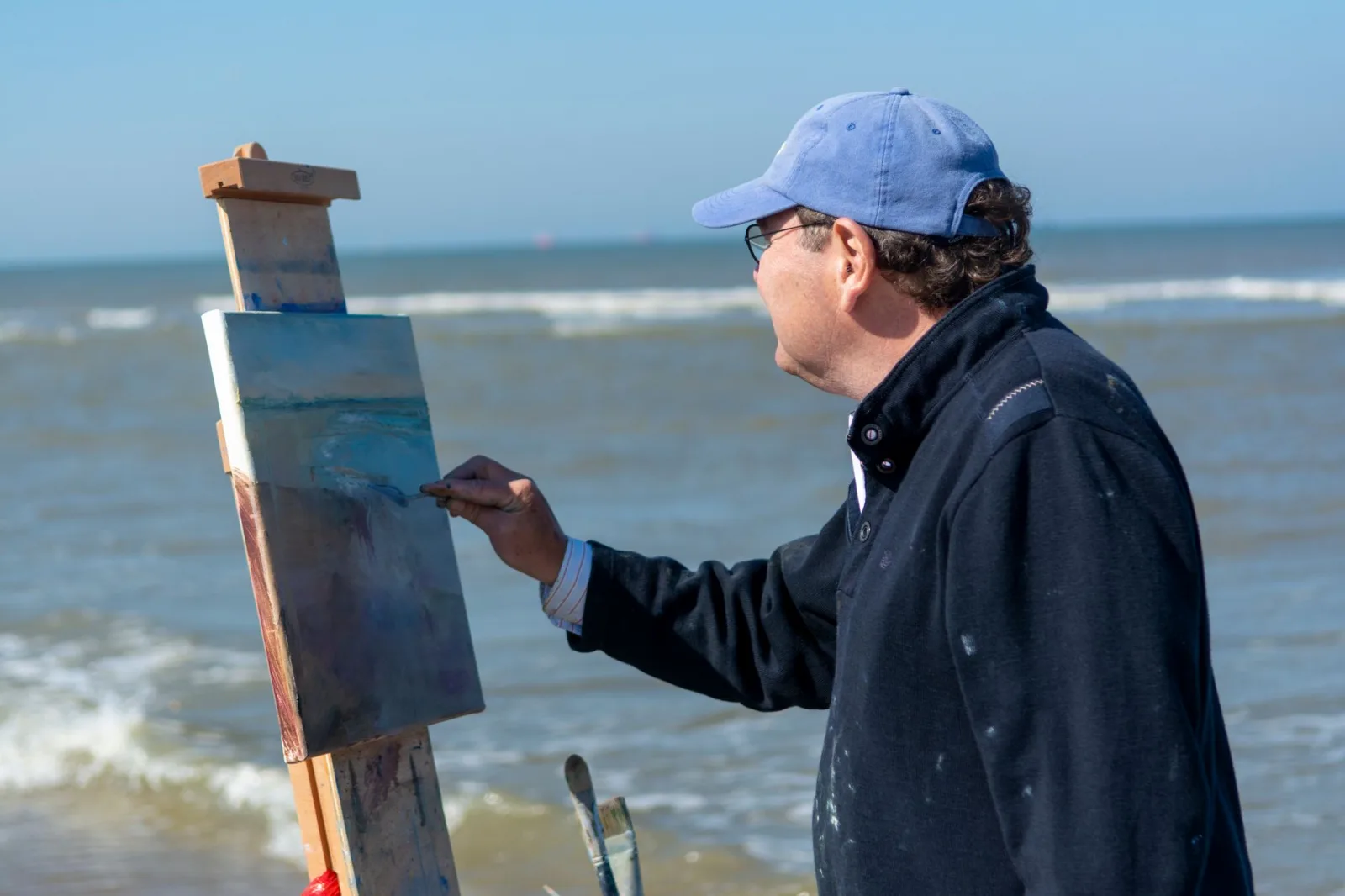 An artist painting a seascape on the beach with an easel, showcasing creative inspiration.