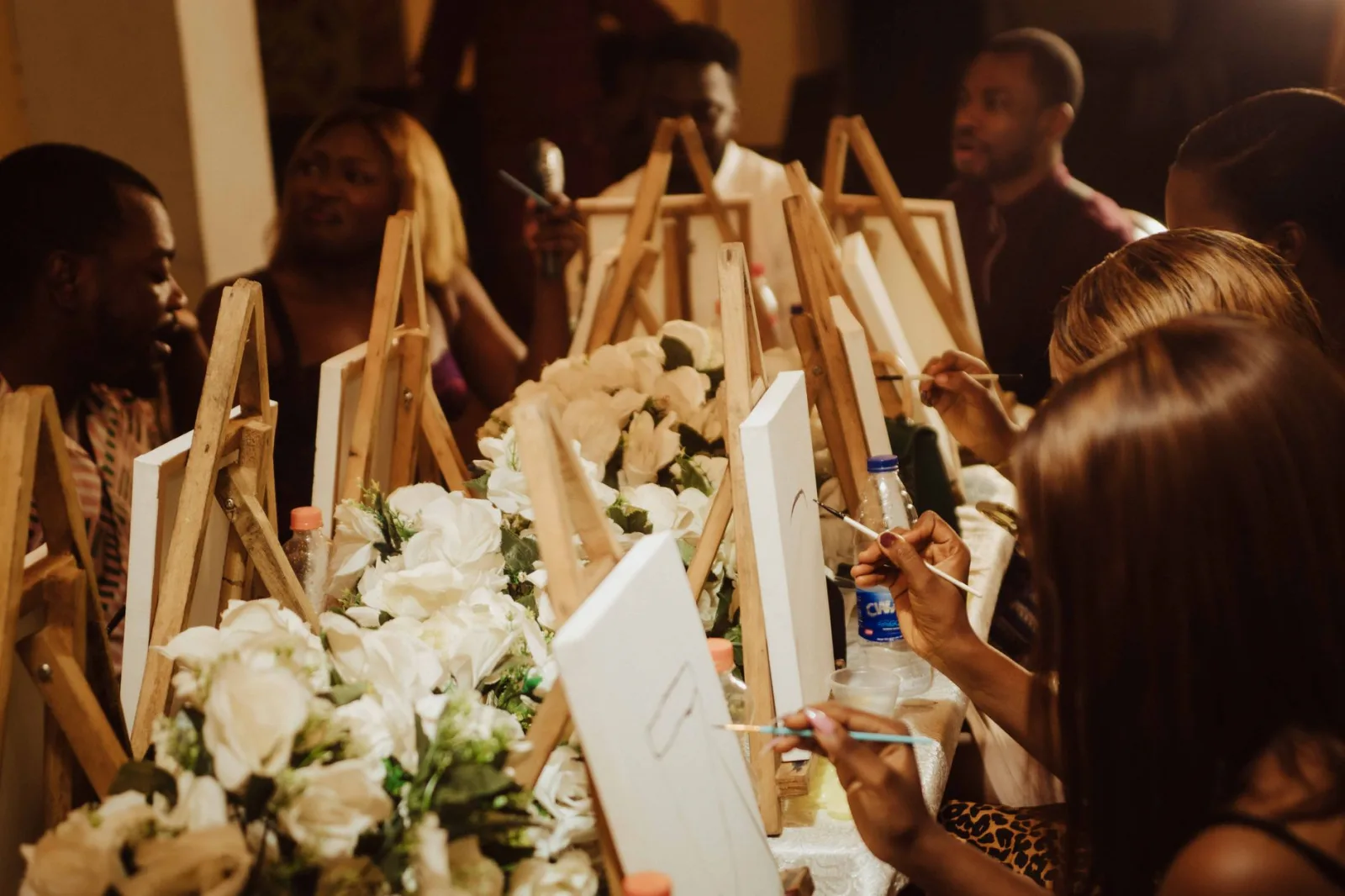 A group of adults engaged in a fun painting session with easels and flowers, captured indoors.
