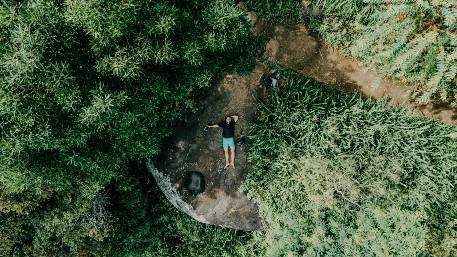 Aerial photo of a person lying on a rock surrounded by lush Sri Lankan jungle.
