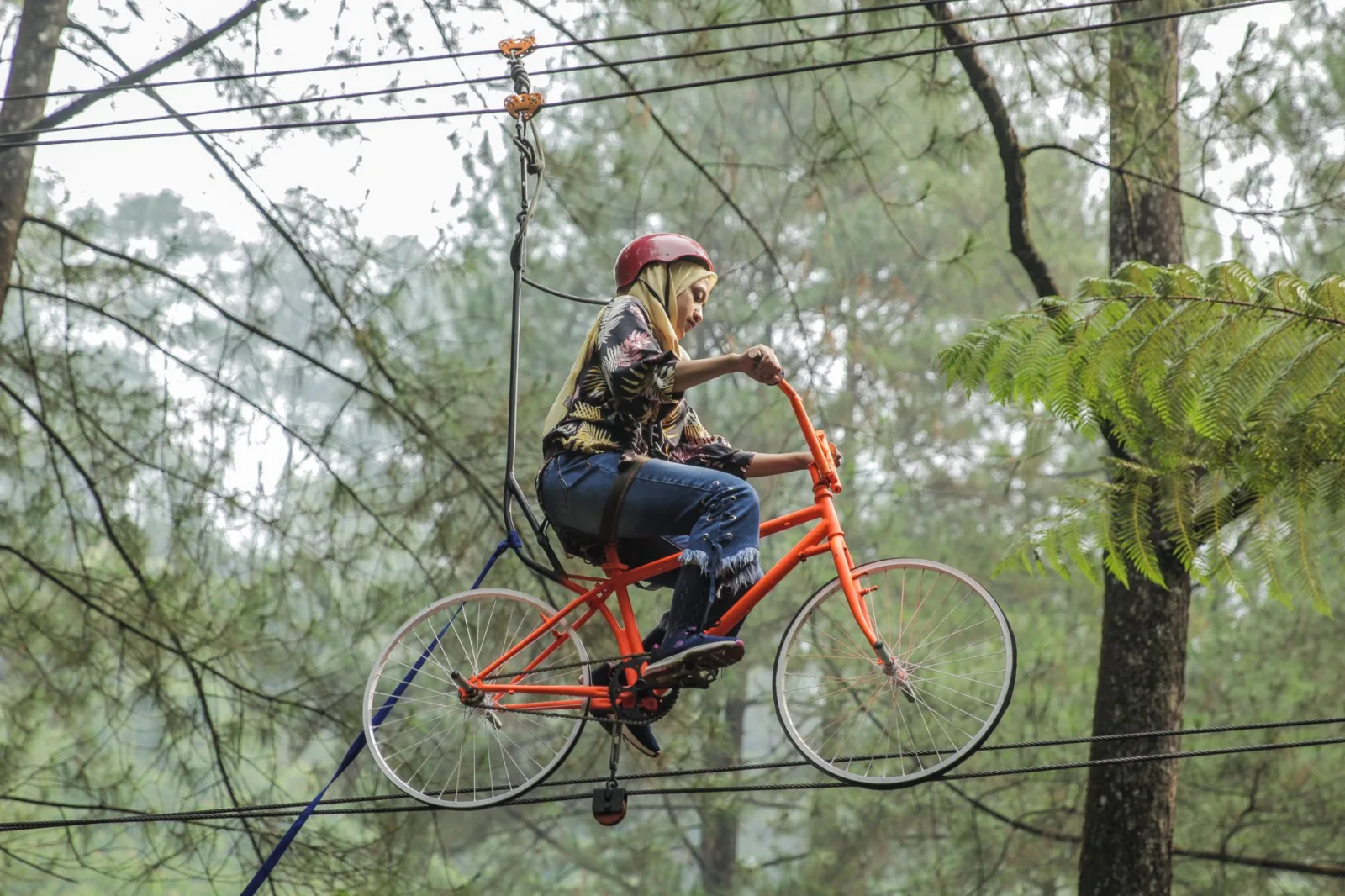 Asian woman rides a high-wire bicycle in the adventurous outdoors.