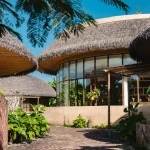 Charming tropical resort architecture with lush greenery and thatched roofs under a clear blue sky.