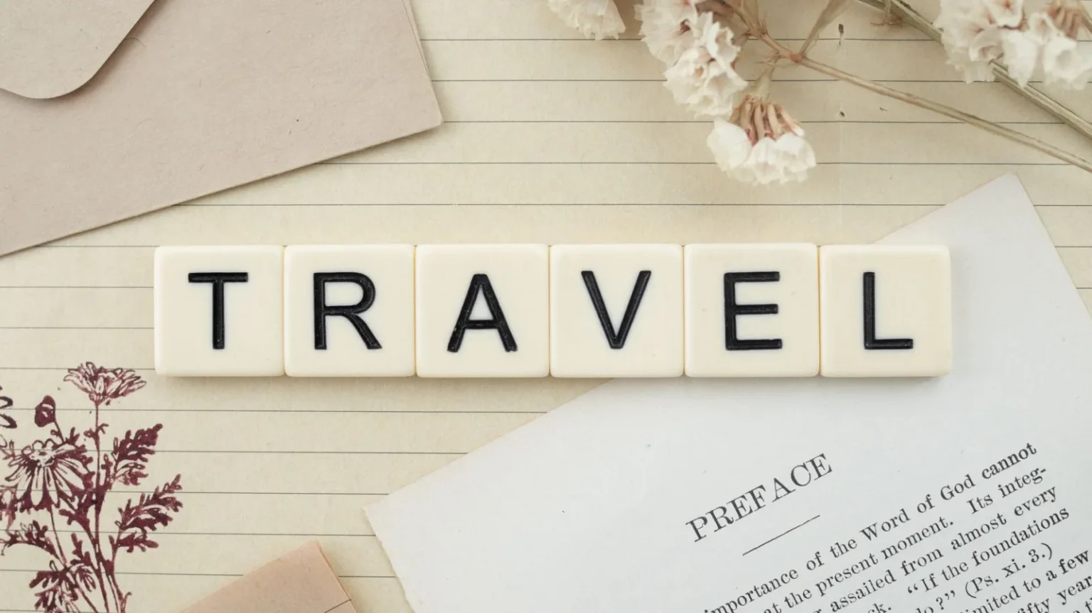 Travel-themed flat lay with Scrabble tiles, dried flowers, and stationery creating a vintage vibe.