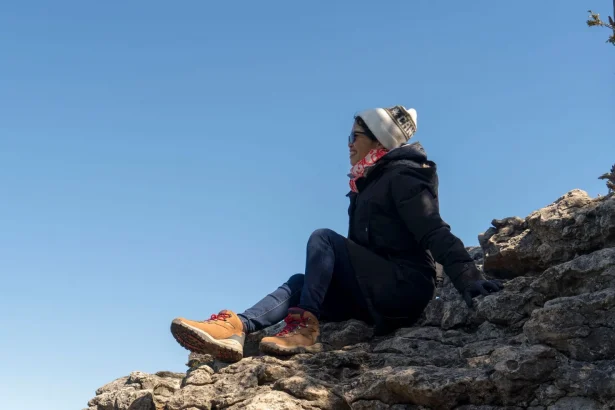 Woman sits on rocky terrain, enjoying a sunny day outdoors, dressed warmly for adventure.