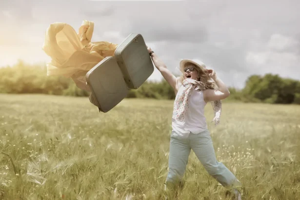 Happy woman in sunny field throwing suitcase joyously, embodying freedom and adventure.