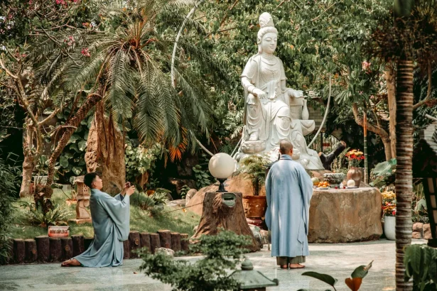 Buddhist monks meditating by a statue in a serene garden setting.